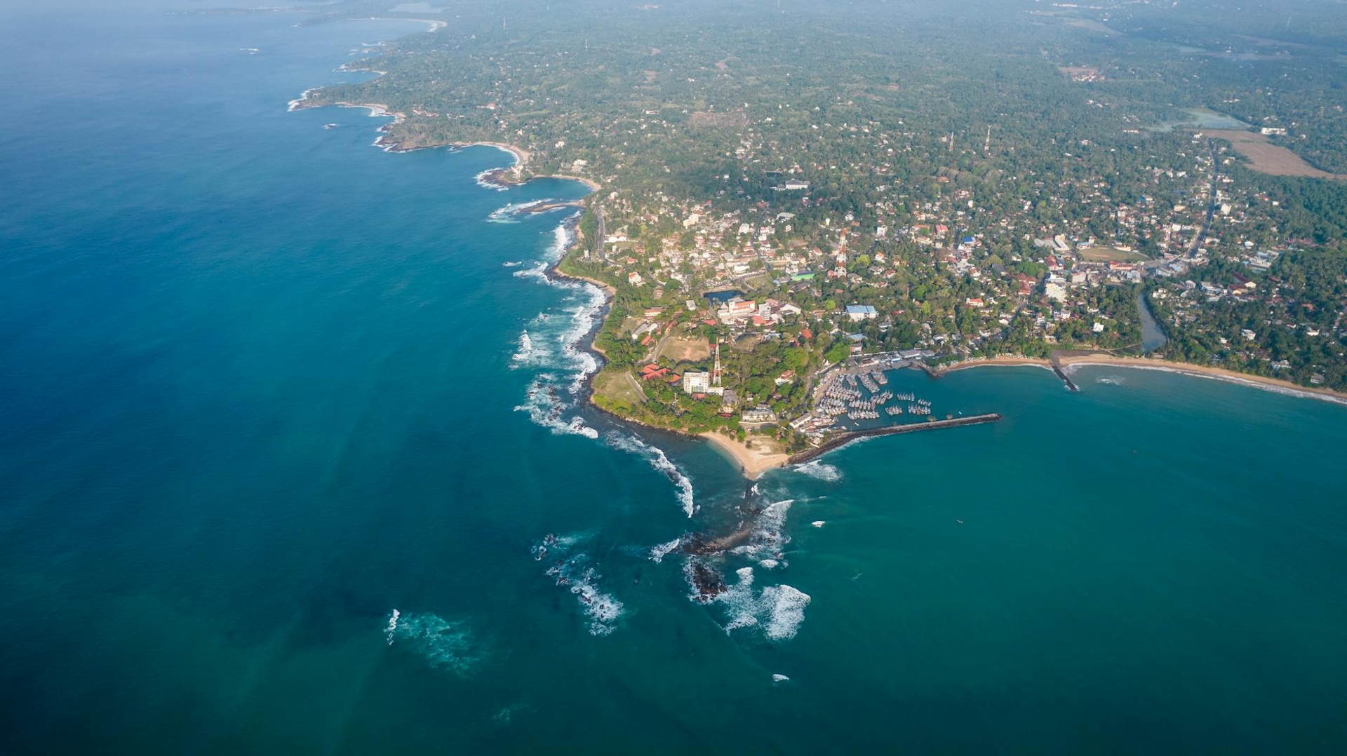 Aerial view of a wooded coastal headland surrounded by blue sea