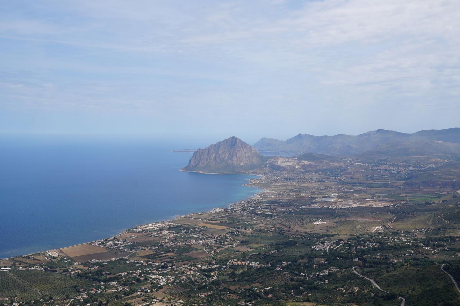 Aerial view of a coastal plain beneath a steep rocky promontory jutting into the sea
