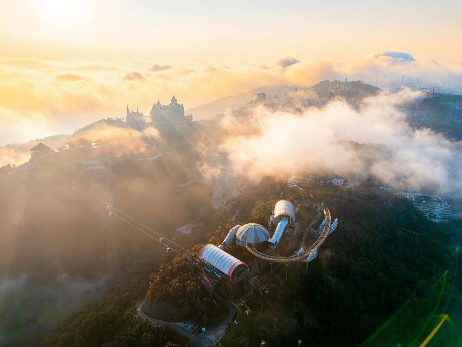 A hilltop cable car station and structures rising above a sea of clouds at sunrise