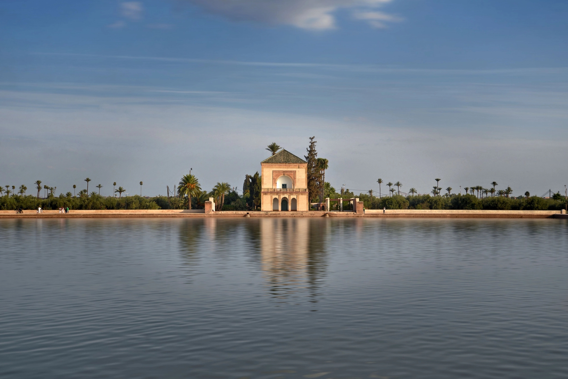 Tranquil view of Menara Gardens pavilion reflecting in water under a clear blue sky in Marrakech