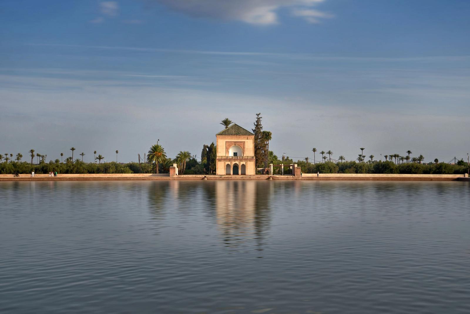 Tranquil view of Menara Gardens pavilion reflecting in water under a clear blue sky in Marrakech