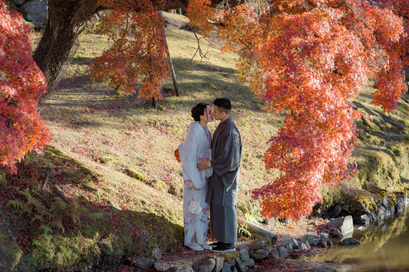 A couple in traditional kimono embracing beneath red autumn maple leaves