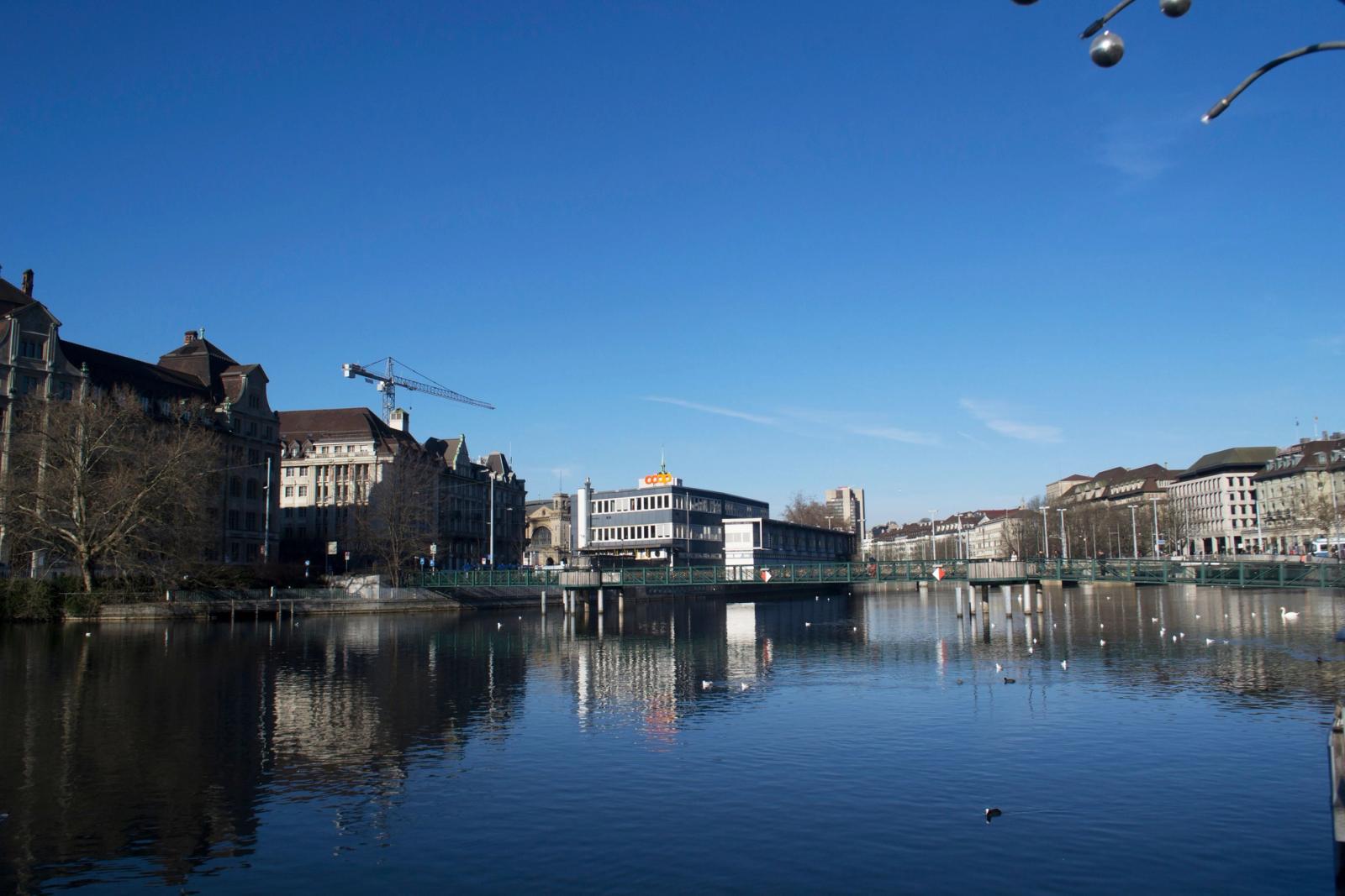 Picturesque scene of Zürich's architecture and waterfront reflecting in the calm river under a clear blue sky