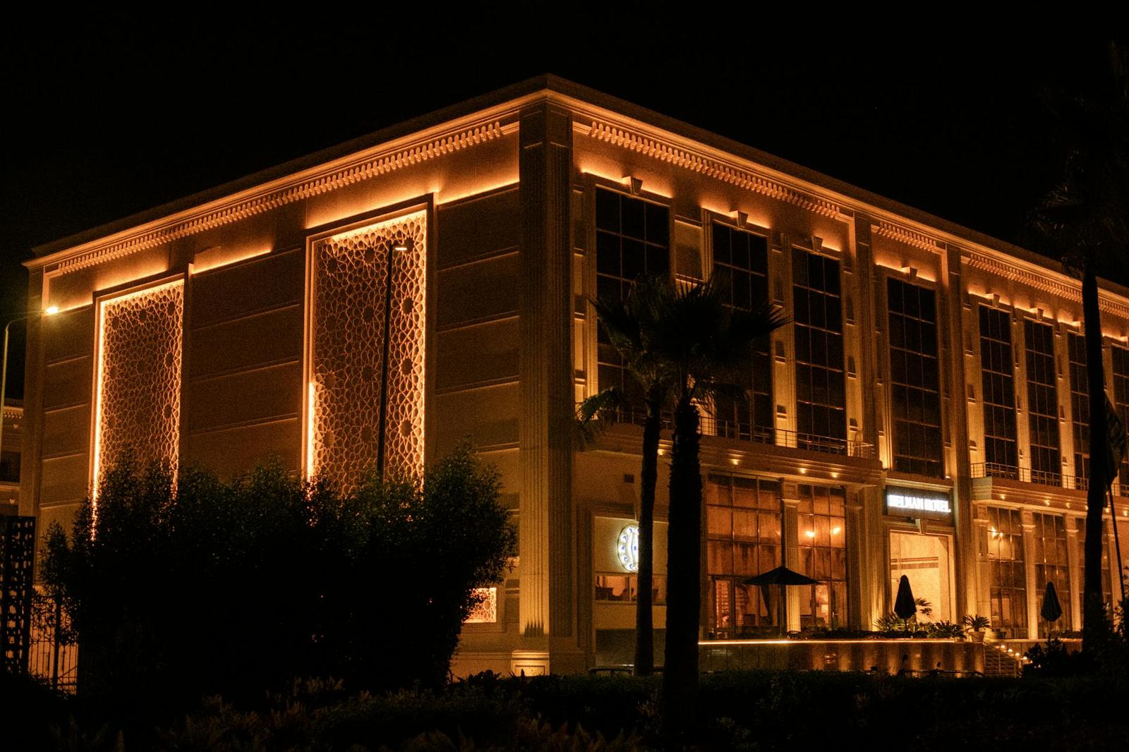 A warmly lit ornate hotel corner with patterned screens and palm trees at night
