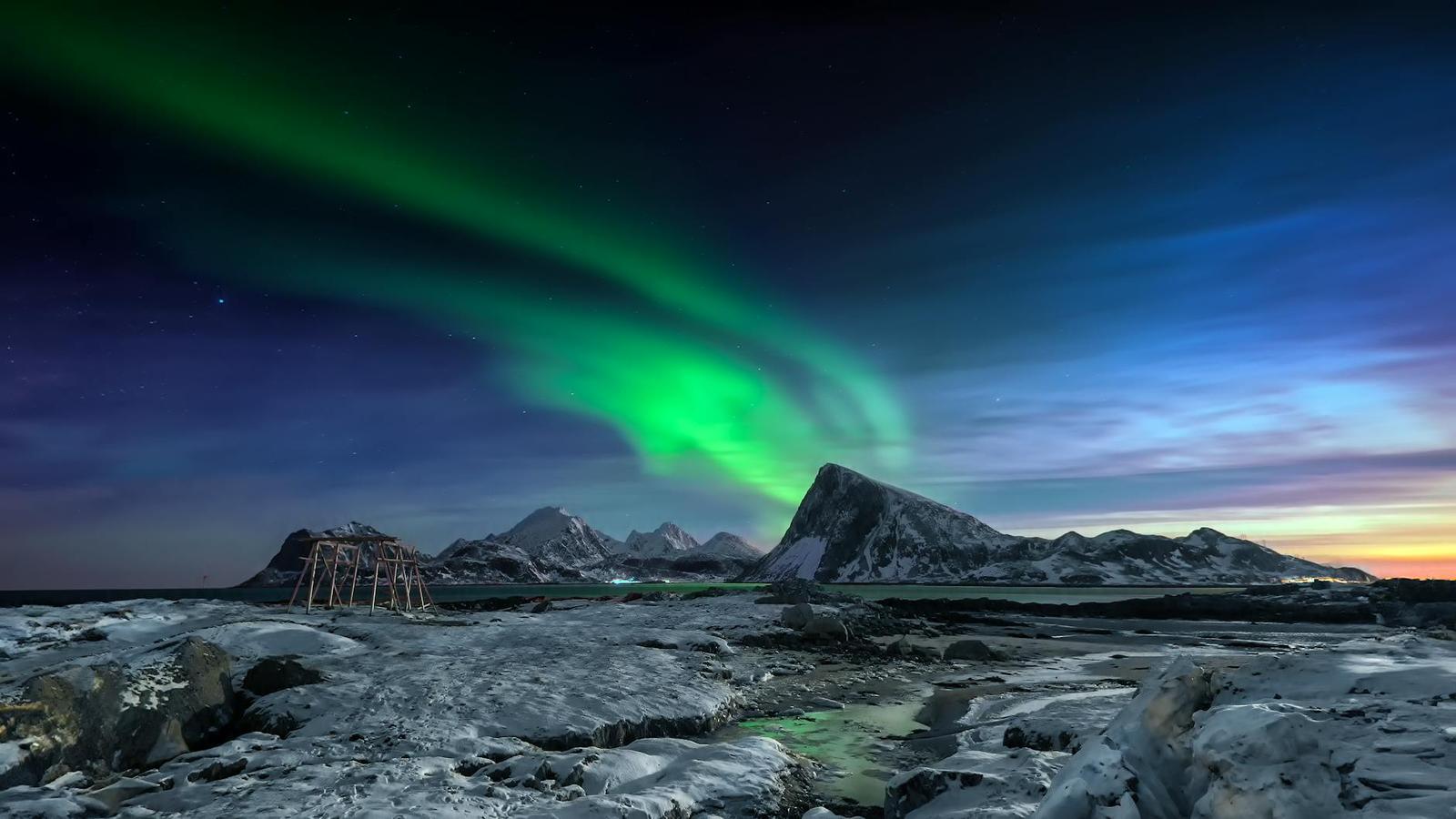 Green aurora arcing over snow-covered peaks and a rock formation