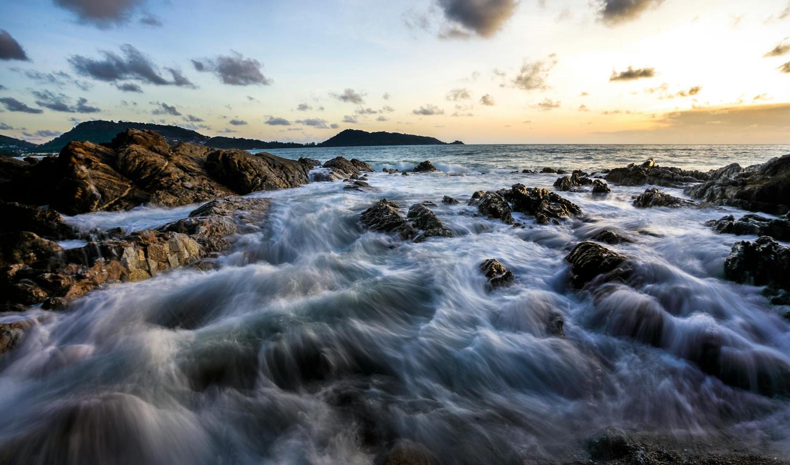 Waves washing over dark rocks along a coastline at sunset