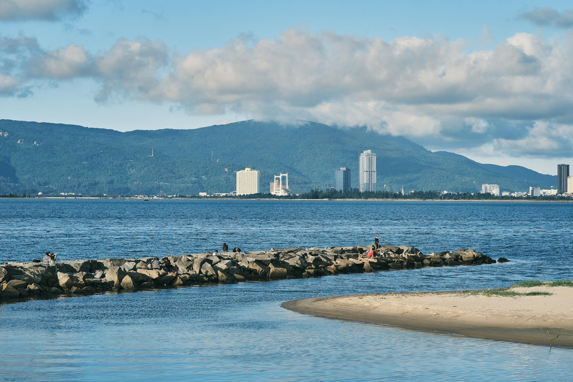 Rocky breakwater stretching into the sea with a hazy city skyline beyond