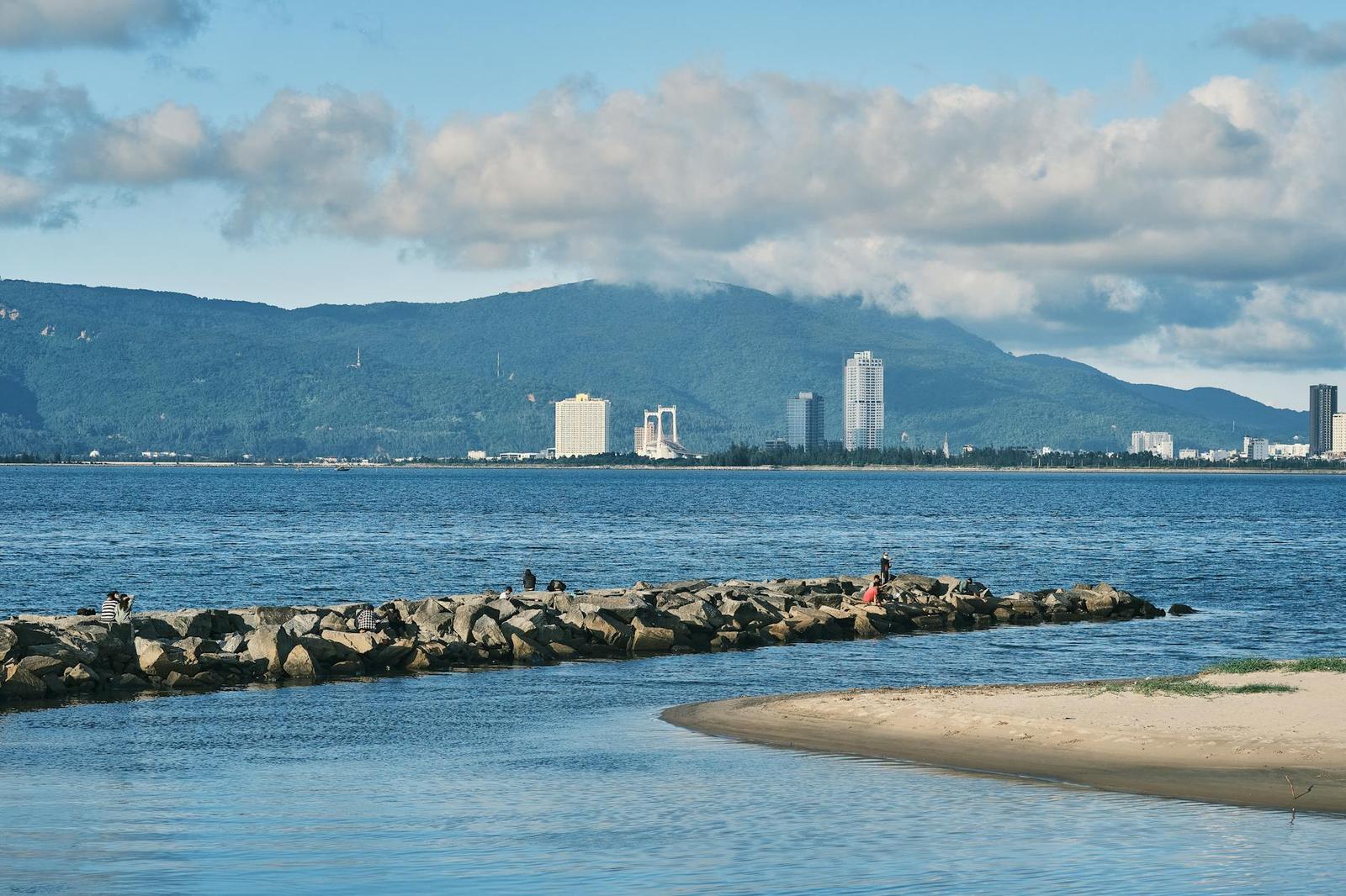 Rocky breakwater stretching into the sea with a hazy city skyline beyond