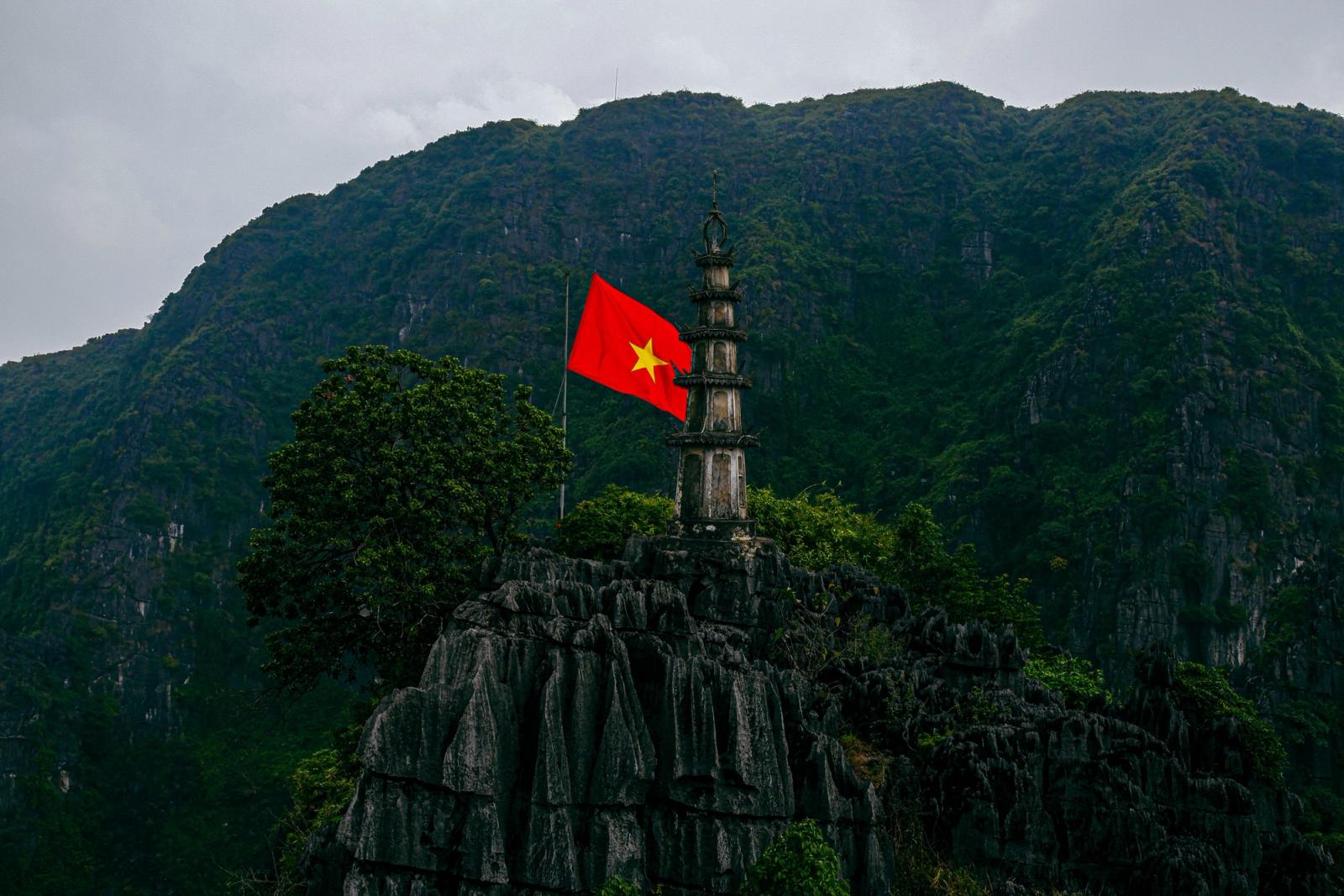 Scenic view of a pagoda and Vietnamese flag atop a mountain in Ninh Bình, Vietnam