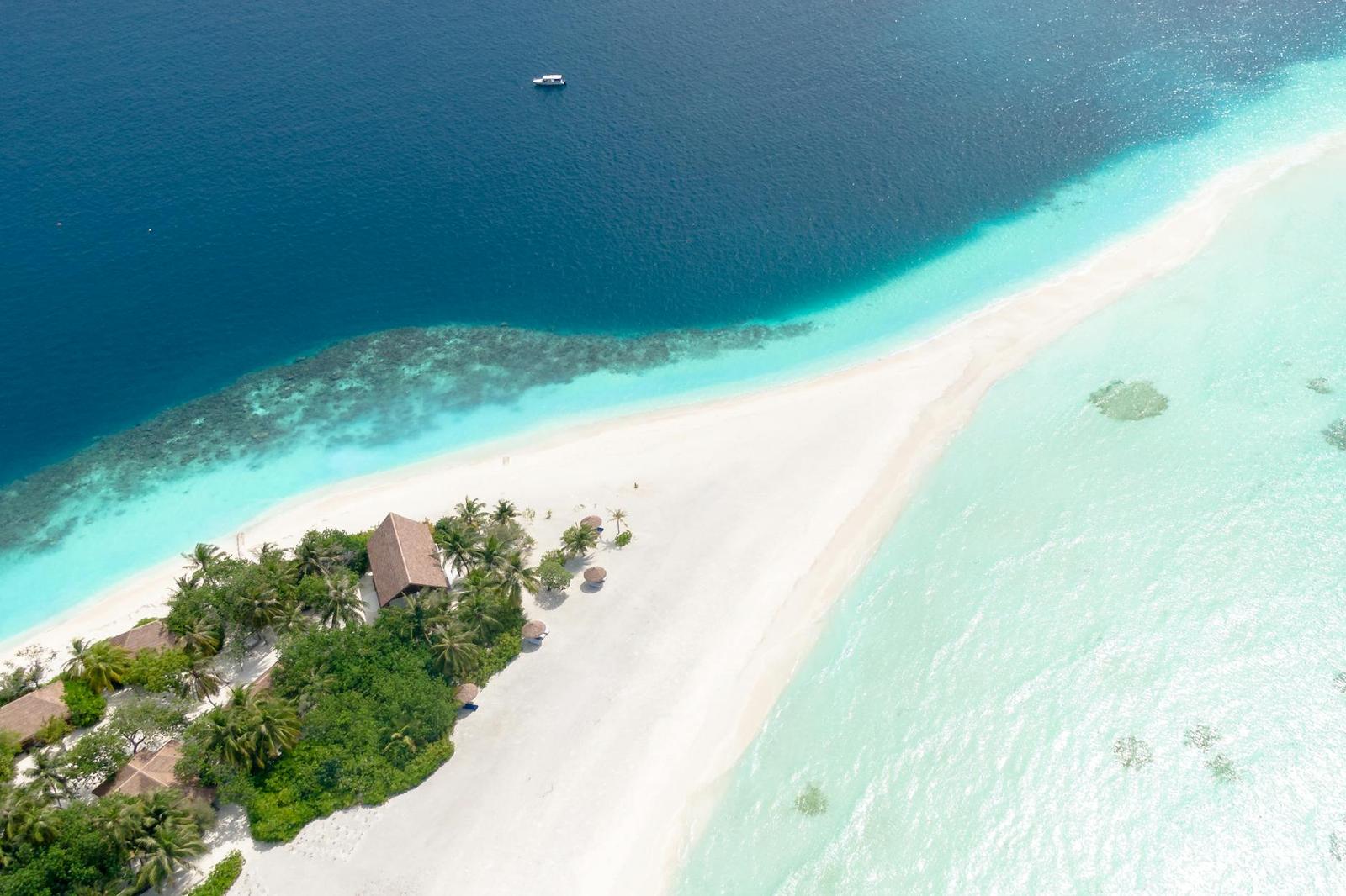Aerial view of a thatched resort house on a narrow sandy point