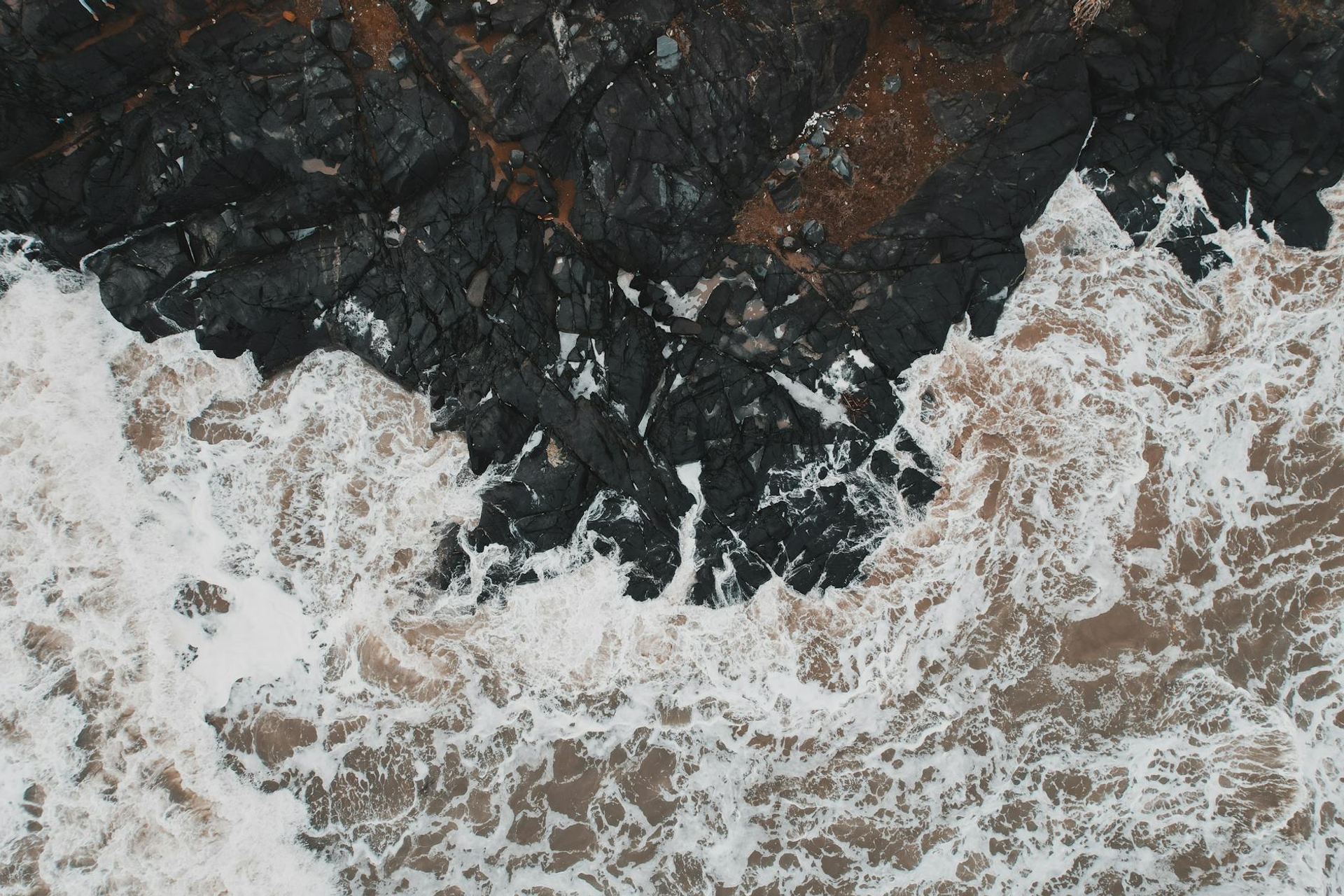 Aerial view of white surf breaking against dark rocky cliffs