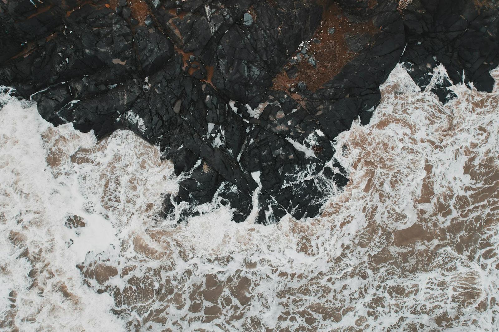 Aerial view of white surf breaking against dark rocky cliffs
