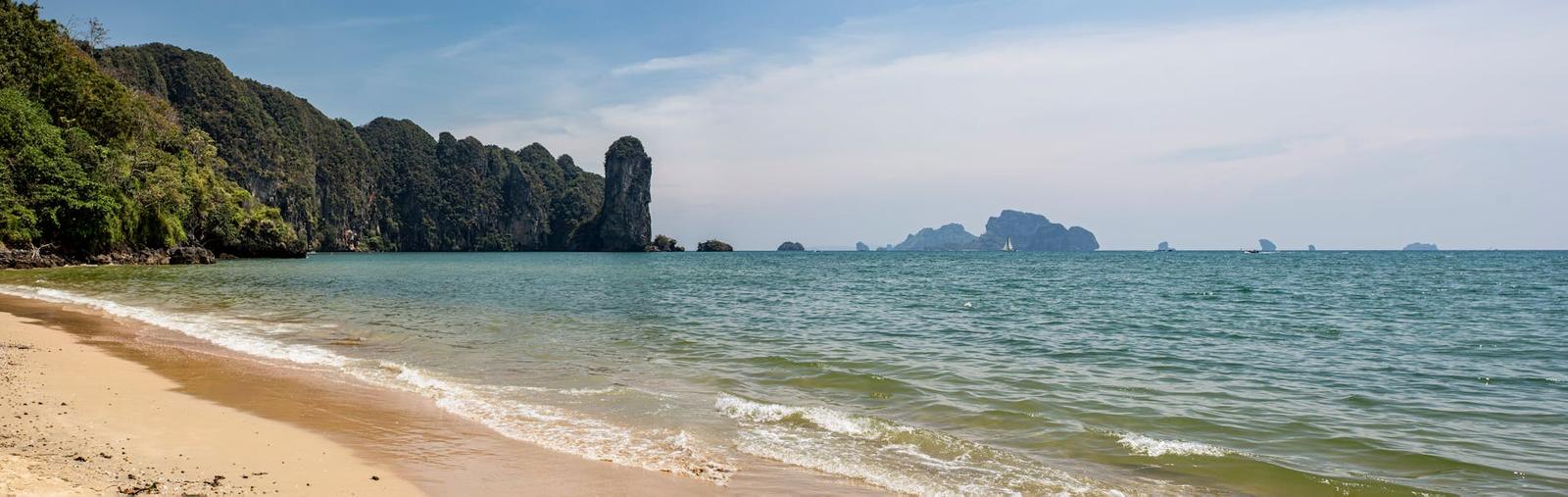 A curved sandy beach beside limestone karst cliffs and distant islands