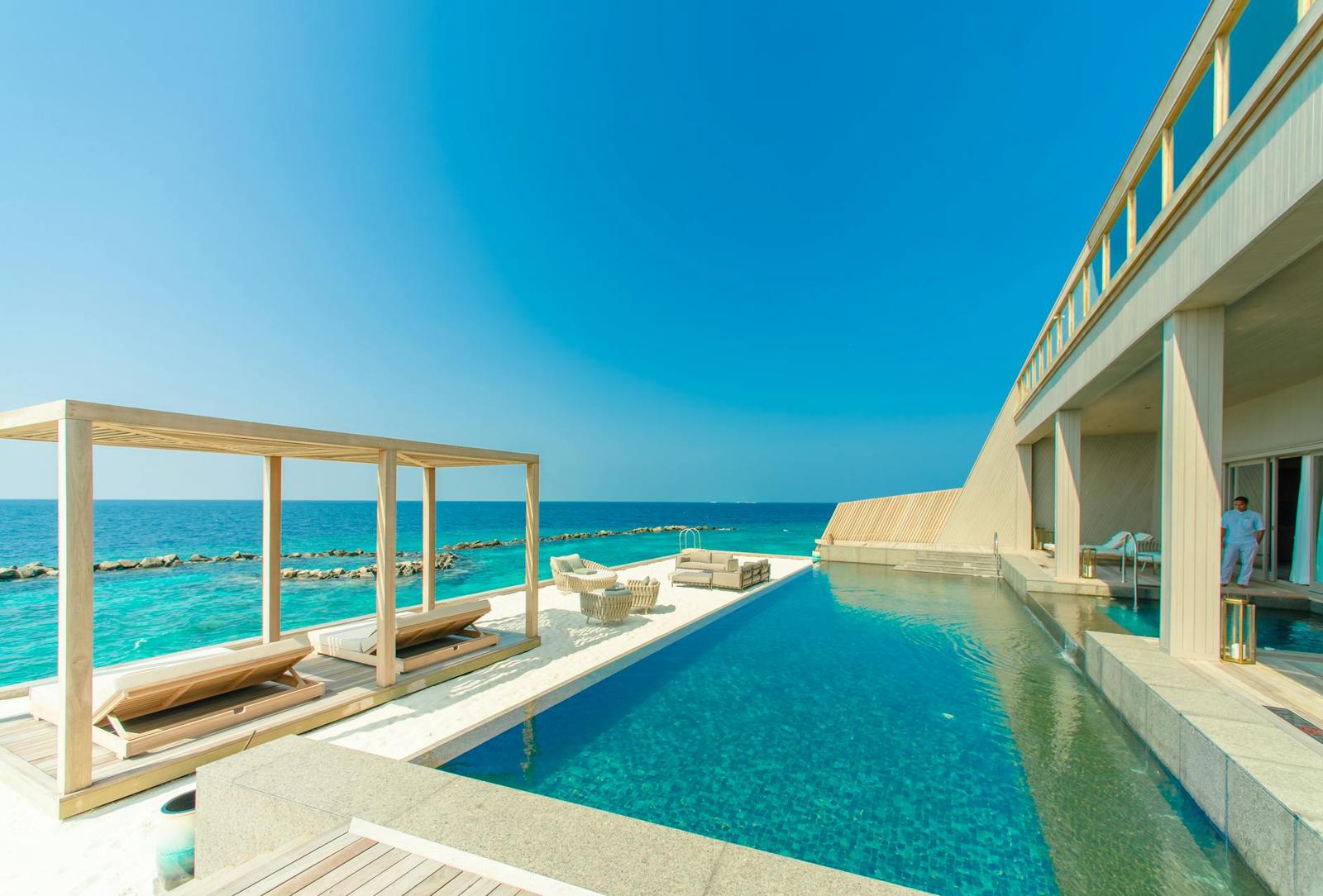 An infinity pool deck beside the ocean with a pergola and lounge chairs