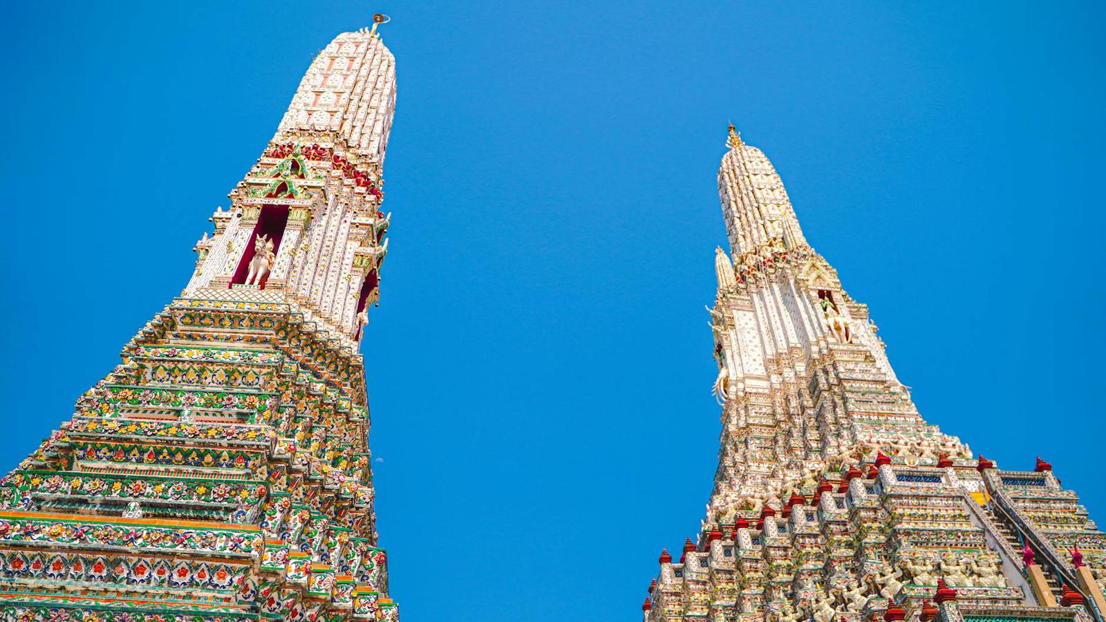 Low angle view of Wat Arun's ornate towers against a clear blue sky in Bangkok, Thailand