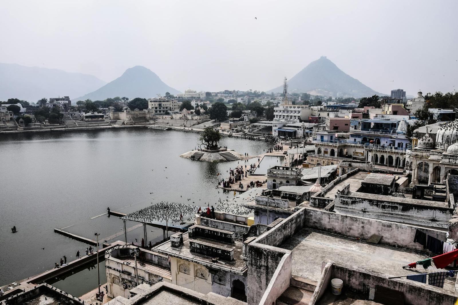 An aerial view of a lakeside town with stepped ghats and distant hills