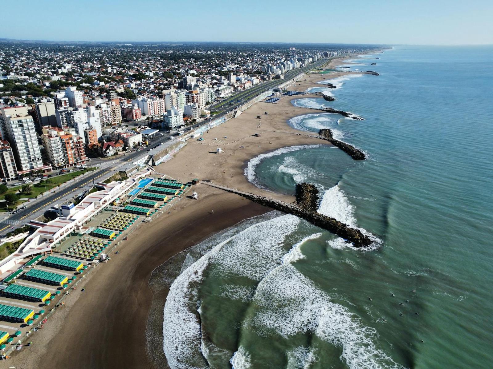 Aerial view of a beach town with striped cabanas and a stone breakwater into the sea