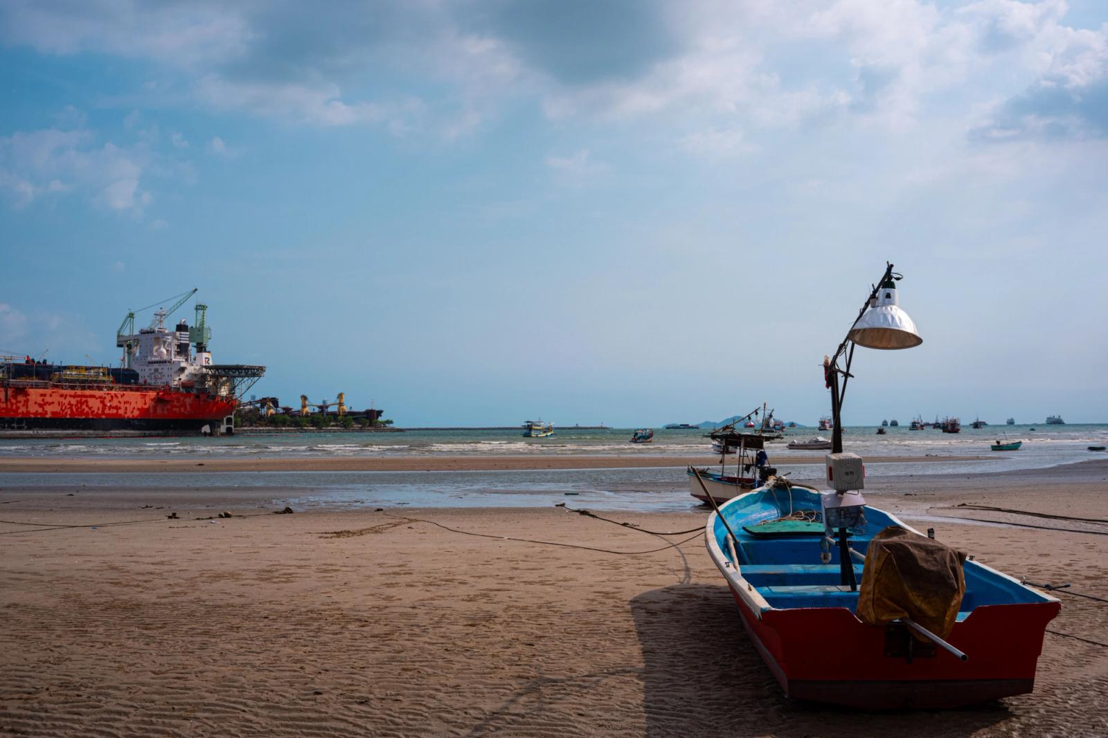 Stunning Pattaya beach view featuring fishing boats and a distant cargo ship under a bright blue sky