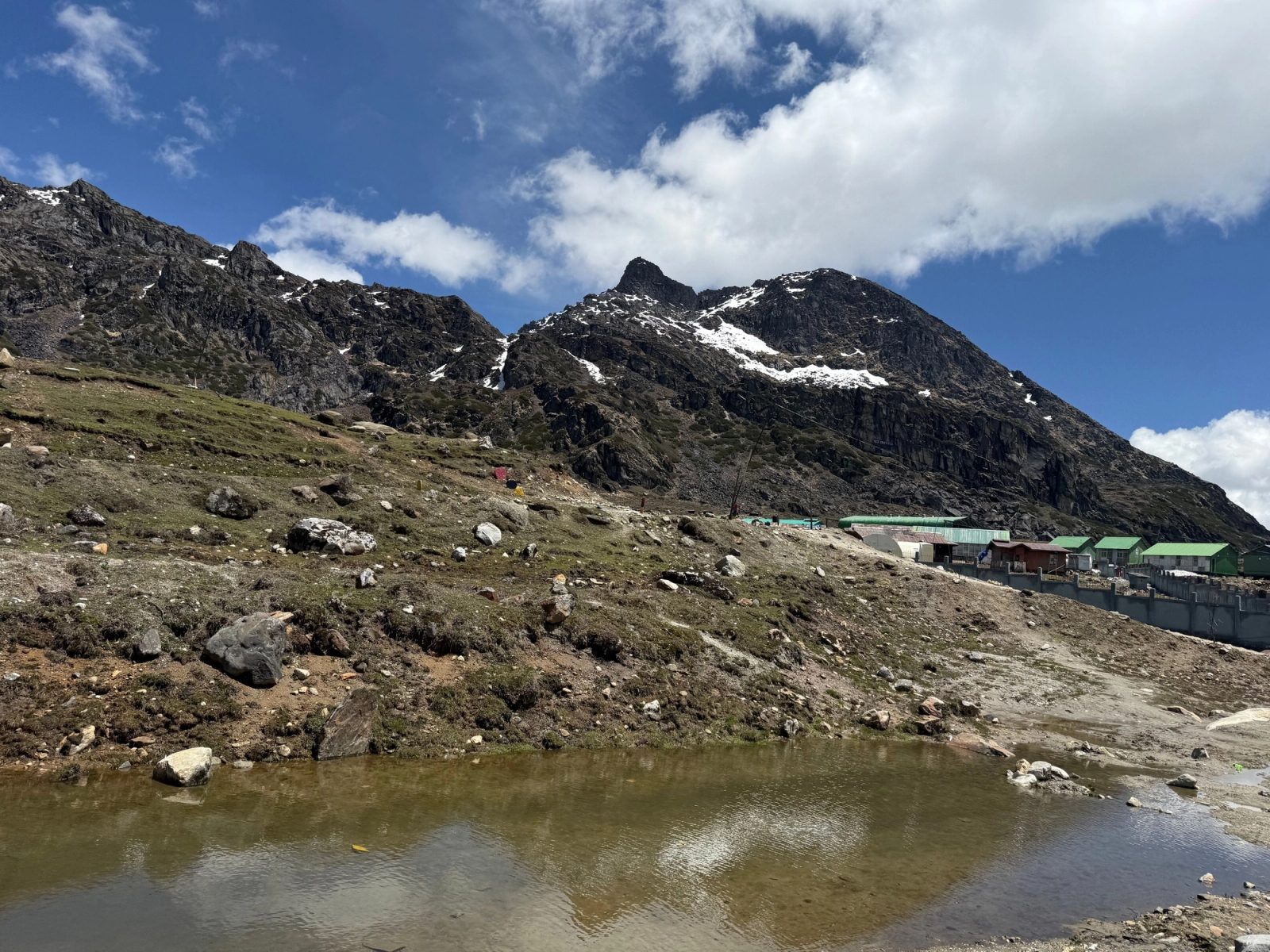 Beautiful mountain landscape in Tawang, India with snow-capped peaks and a tranquil pond under blue skies