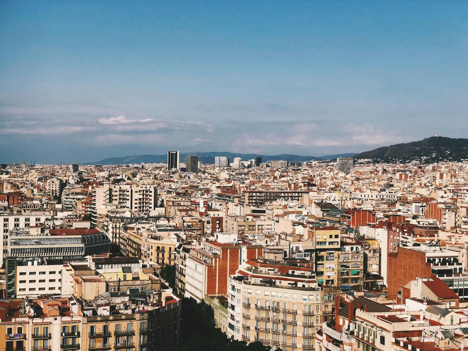 City rooftops sprawling toward distant hills under a blue sky