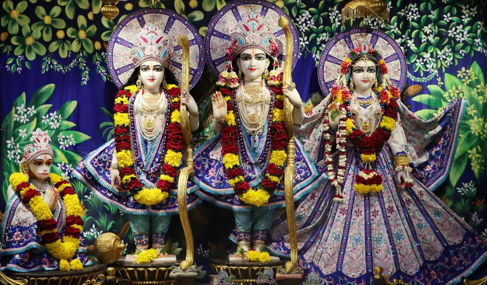 A group of decorated deity idols in colourful robes against a floral backdrop