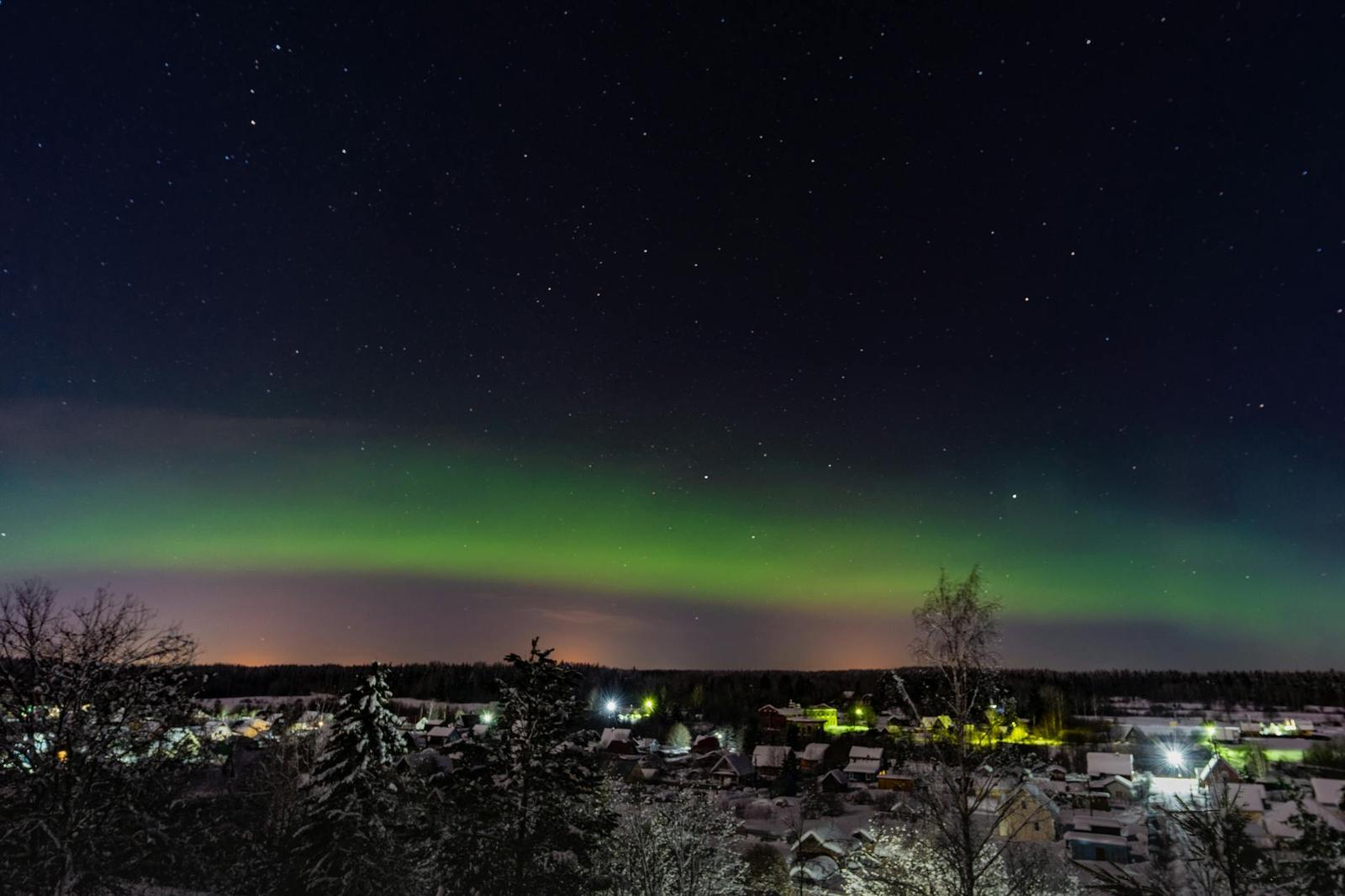 Green aurora glowing above a snow-covered town at night