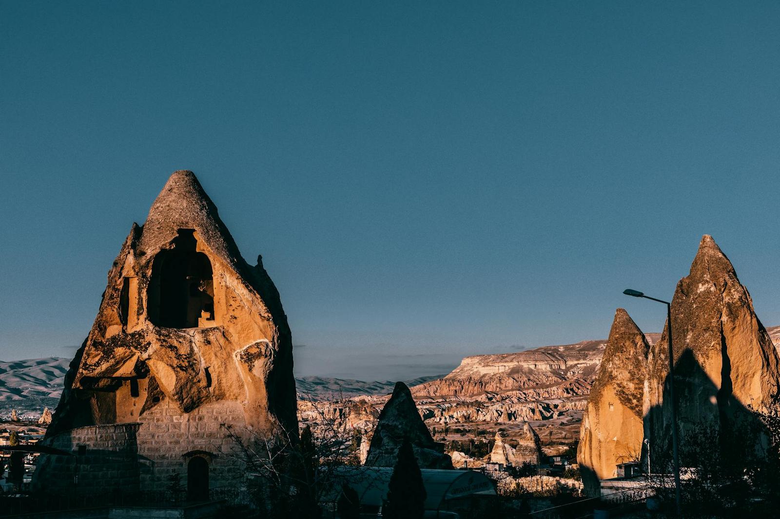 Famous rocky formations with holes and rough surface located in ancient Cappadocia town near hilly terrain against blue sky in Turkey