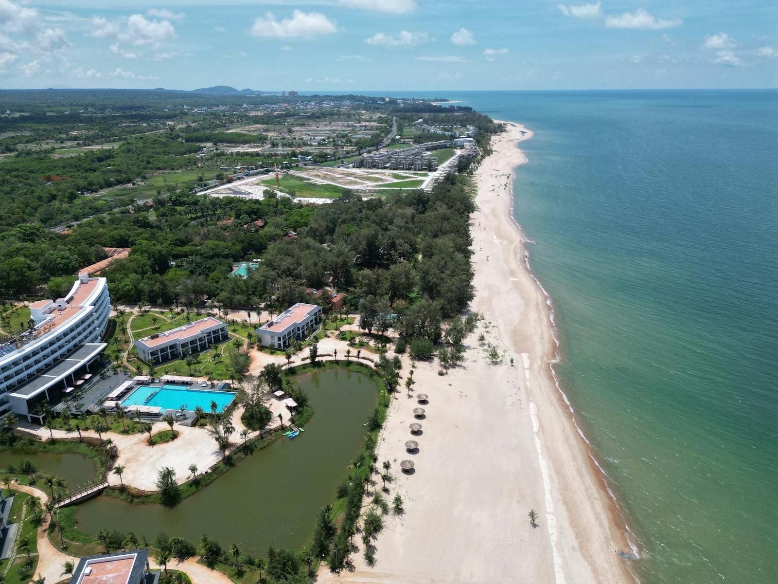 Aerial view of a low-rise beach resort with a pool beside a long sandy shoreline
