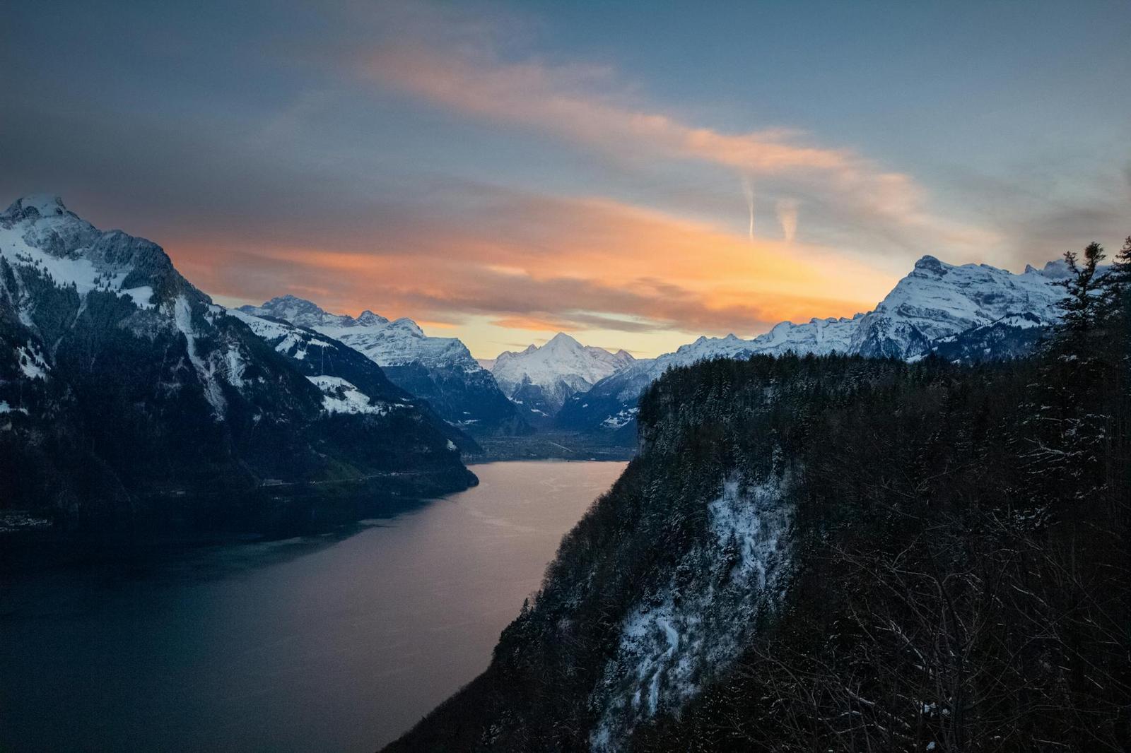 Fjord-like alpine lake glowing orange between snow-capped ridges at sunset