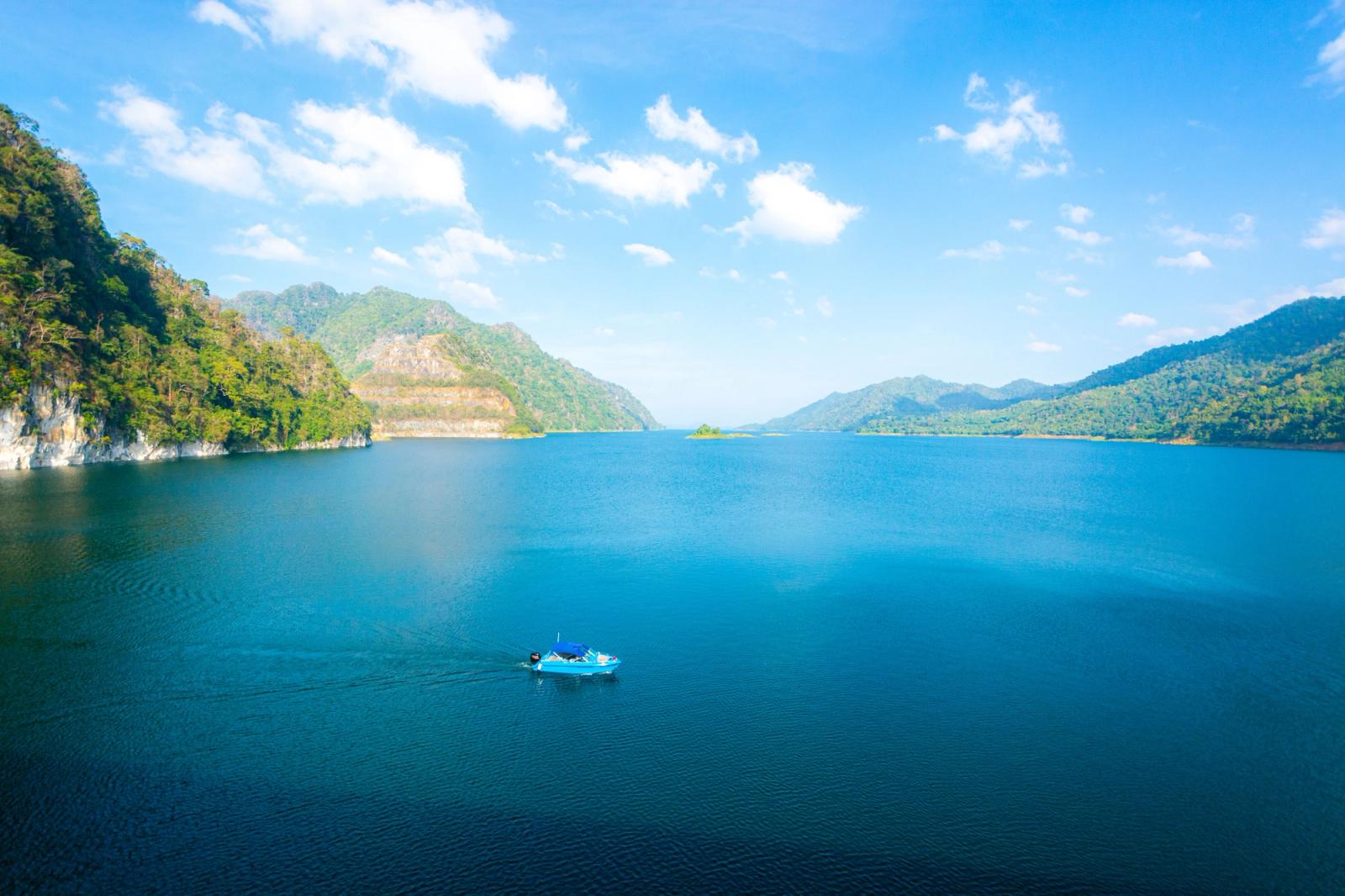 A tranquil view of a blue lake surrounded by lush green hills under a clear sky in Thailand