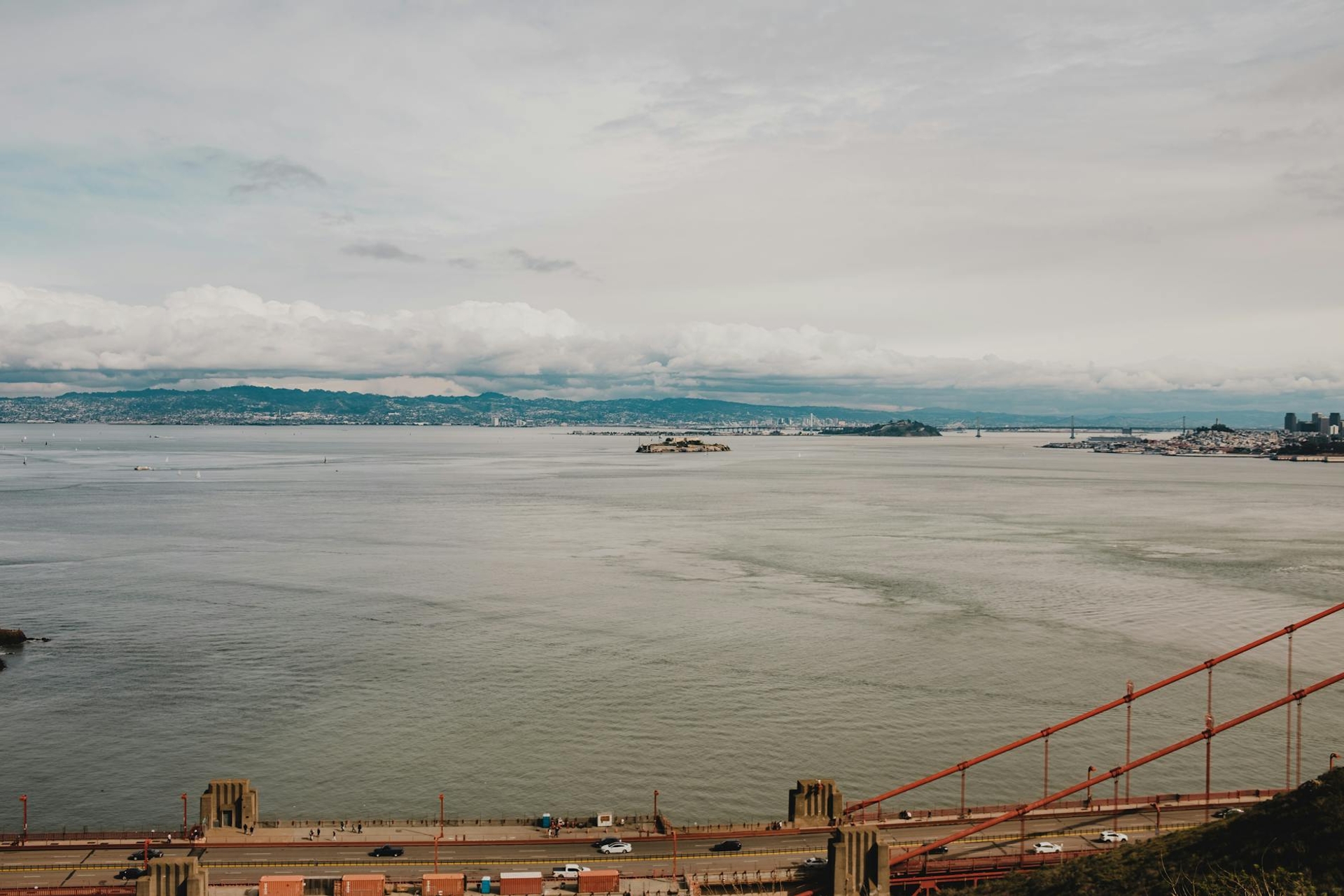 A wide grey bay seen past the red cables of a suspension bridge