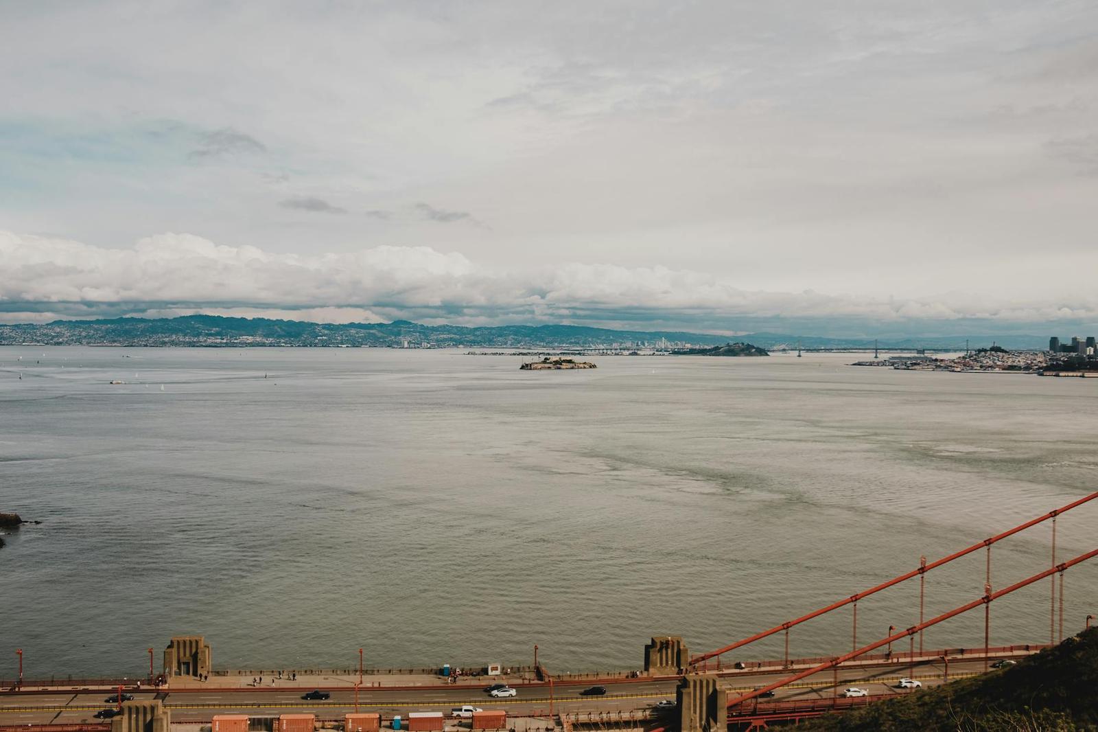 A wide grey bay seen past the red cables of a suspension bridge
