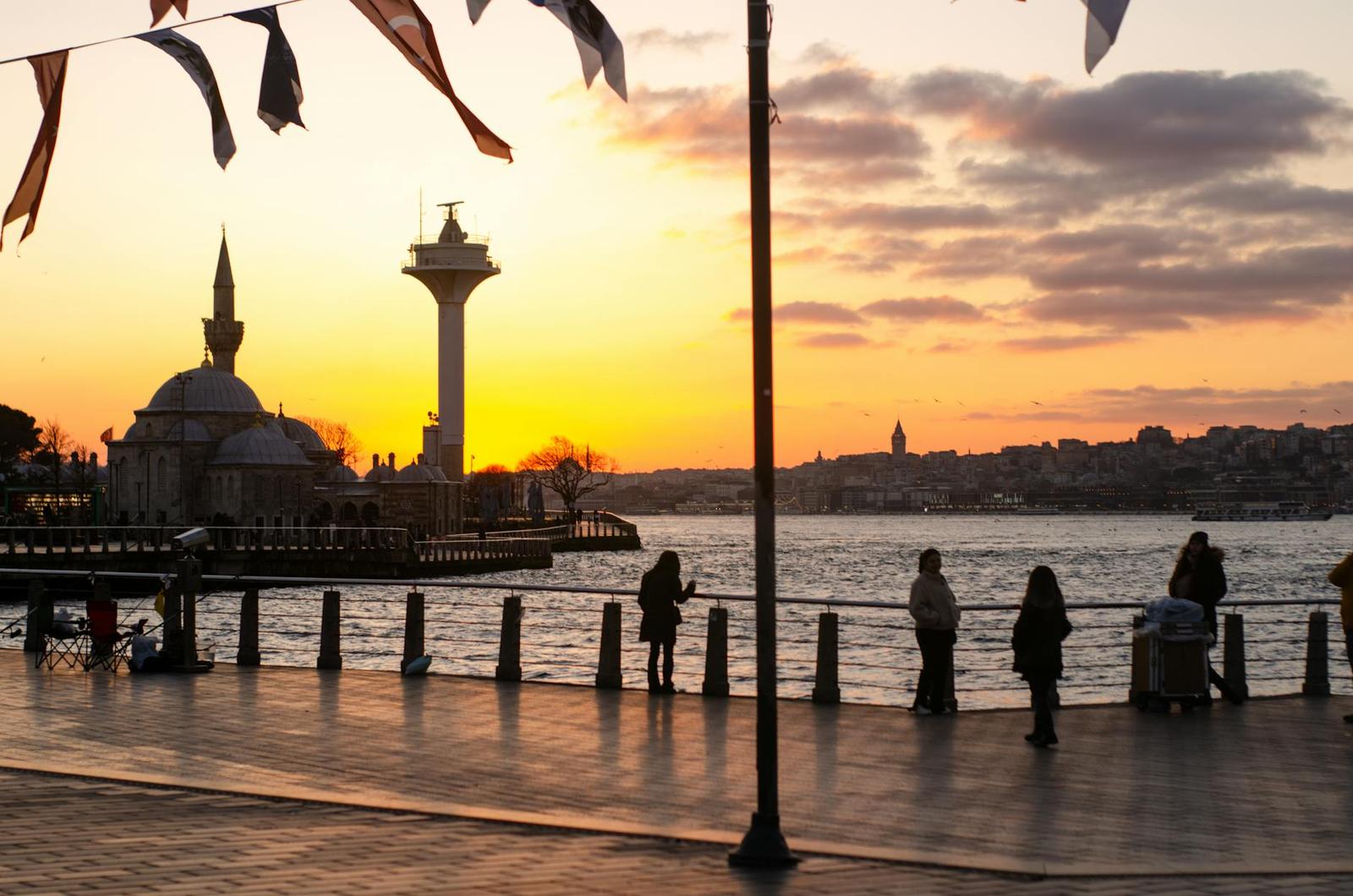 Silhouetted figures along a waterfront promenade watching the sunset
