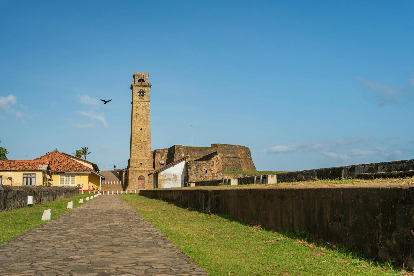 Stone clock tower and fort walls along a grassy path under blue sky
