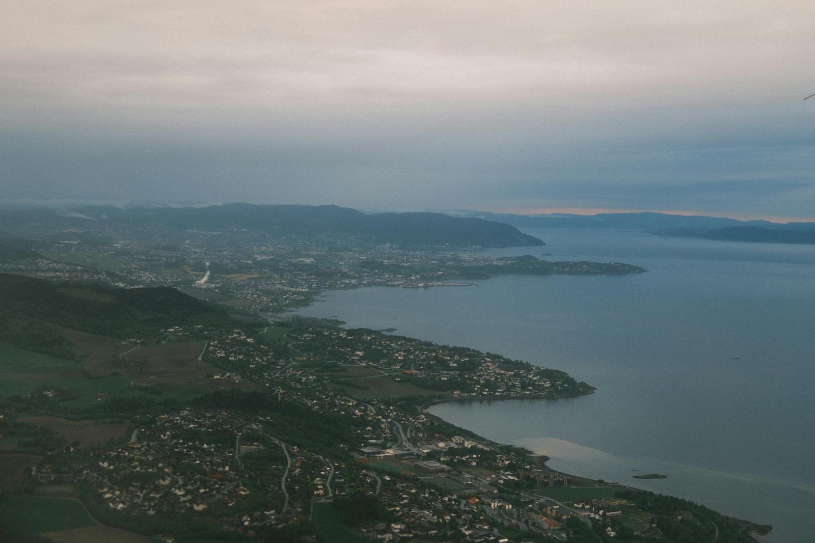 Aerial view of a fjord town spread along the water under grey sky