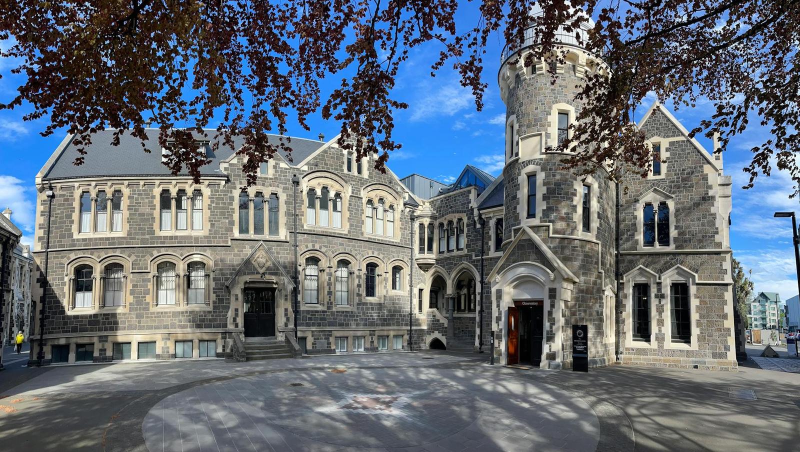 A Gothic revival stone building with a round turret under bare autumn branches
