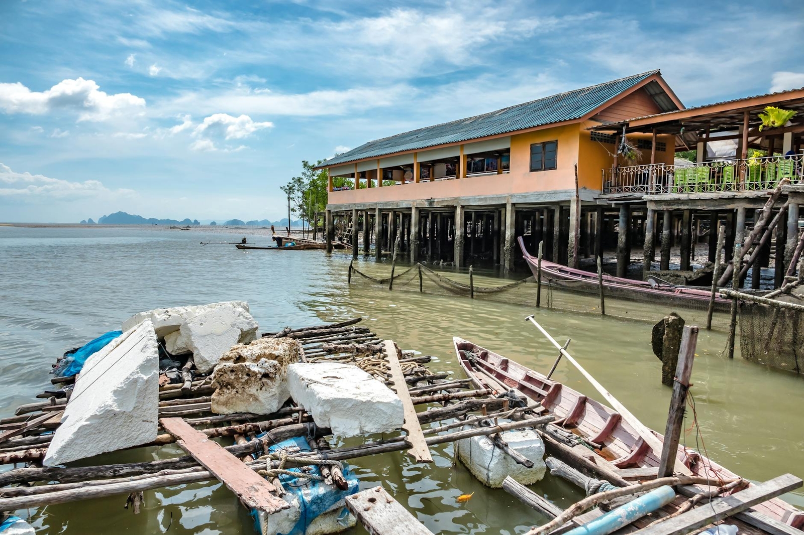 A weathered stilt building over shallow water beside moored wooden boats