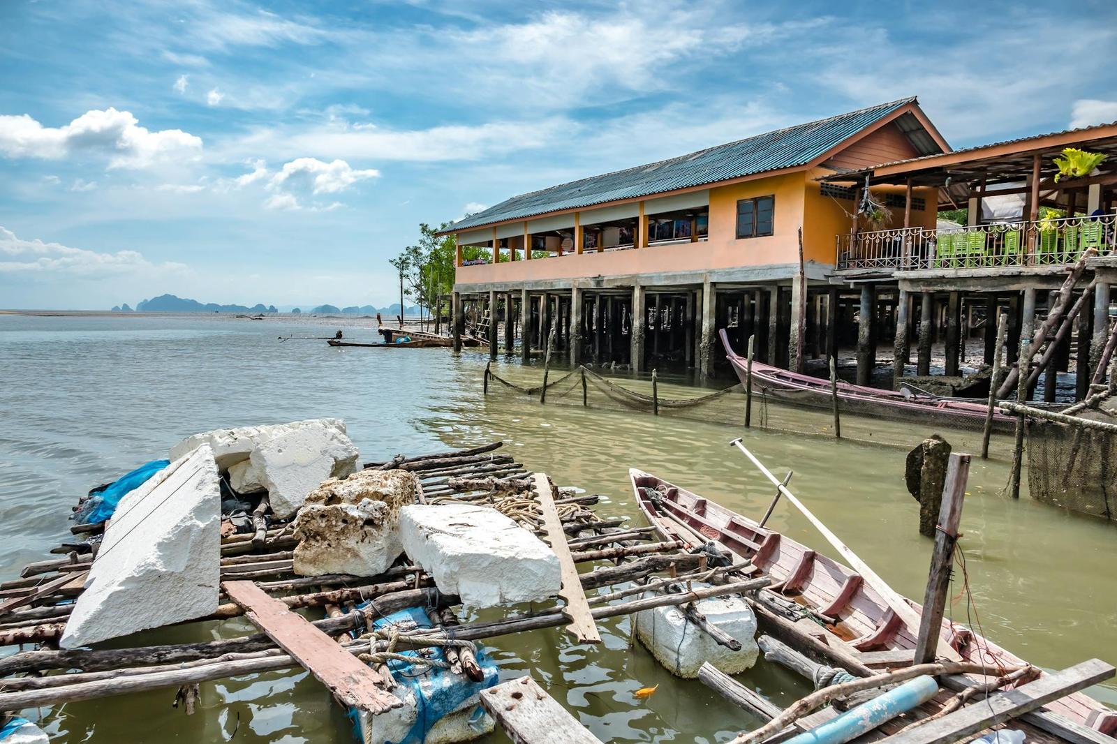 A weathered stilt building over shallow water beside moored wooden boats