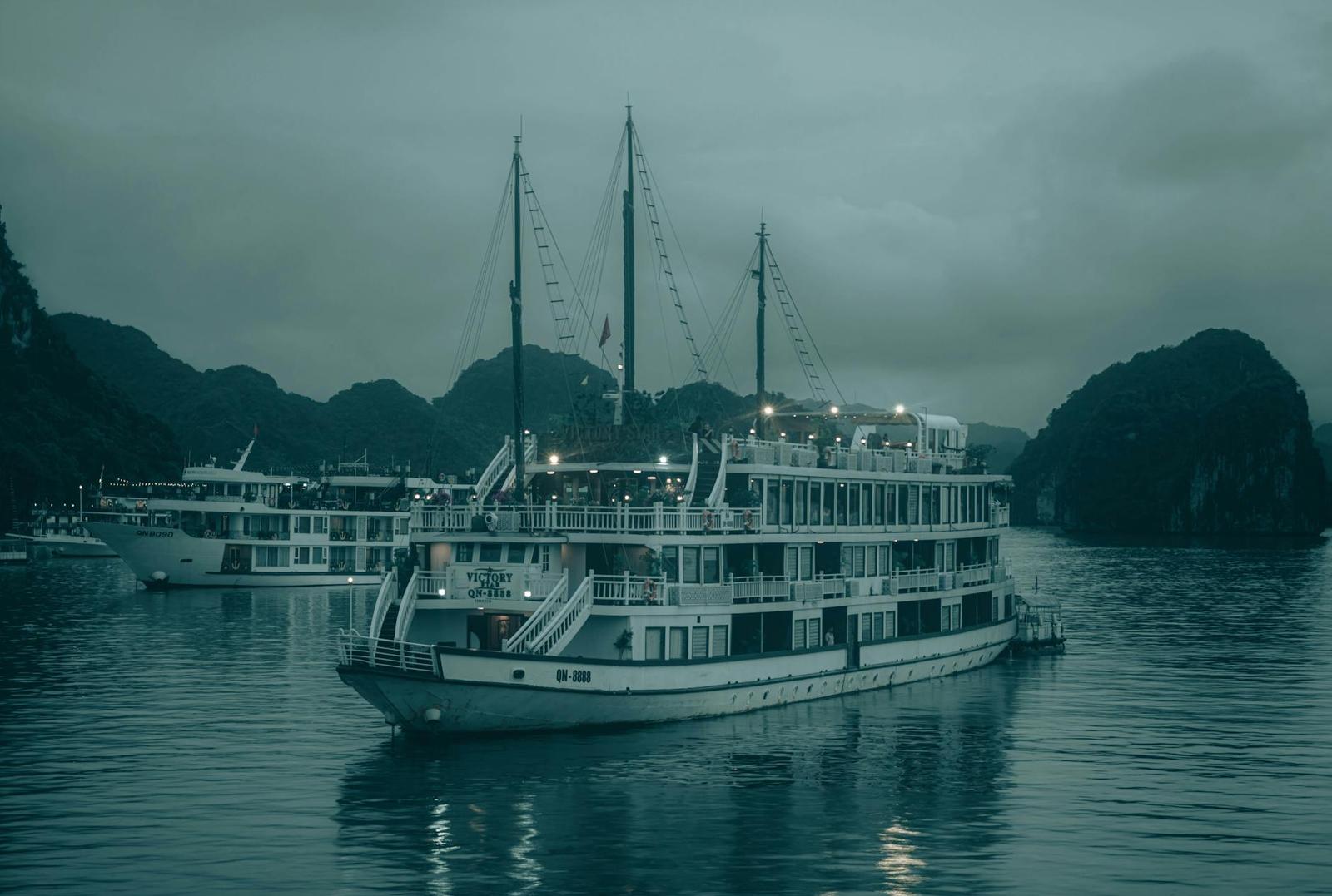 A lit multi-deck cruise boat anchored among limestone islands at dusk