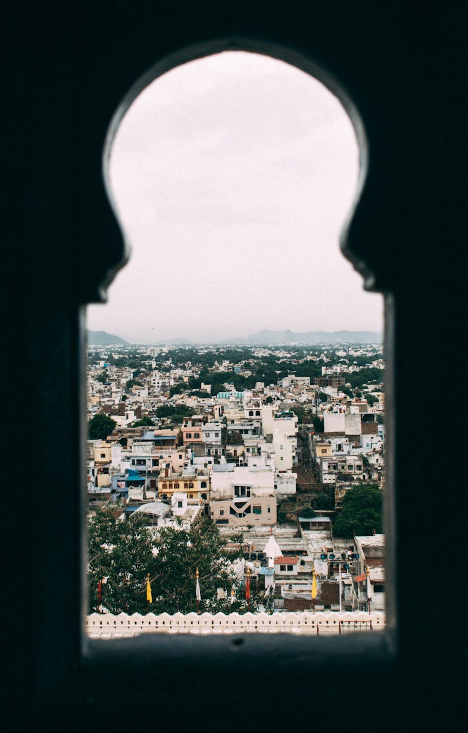 Moorish-arched window overlooking a sprawling city under overcast sky