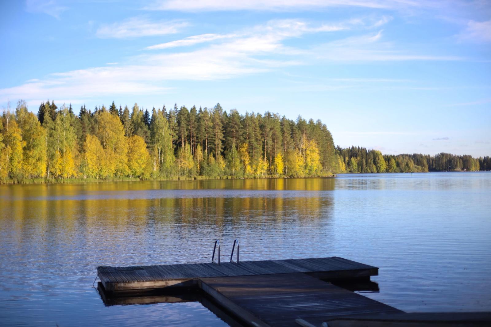 Peaceful autumn lake scene in Finland with dock and vibrant foliage reflecting on the water