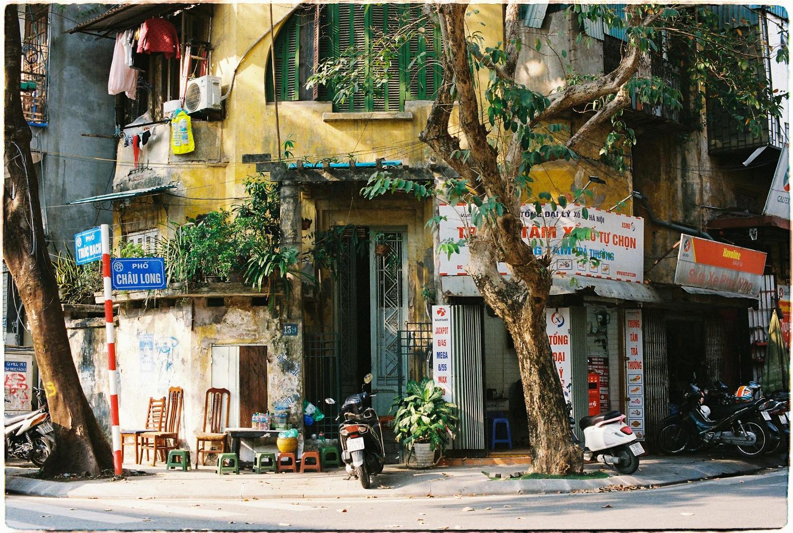 Weathered old-quarter shophouse with motorbikes parked beneath overhanging trees