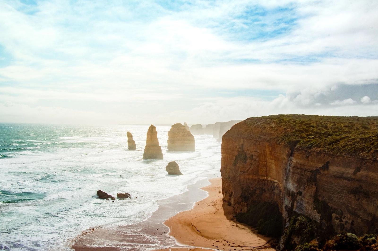 Sea stacks rising from surf below layered sandstone cliffs at dusk