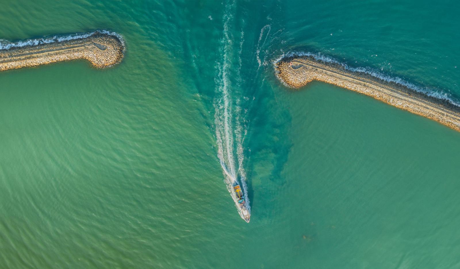 Aerial view of a jet ski cutting through a channel between two curved breakwaters