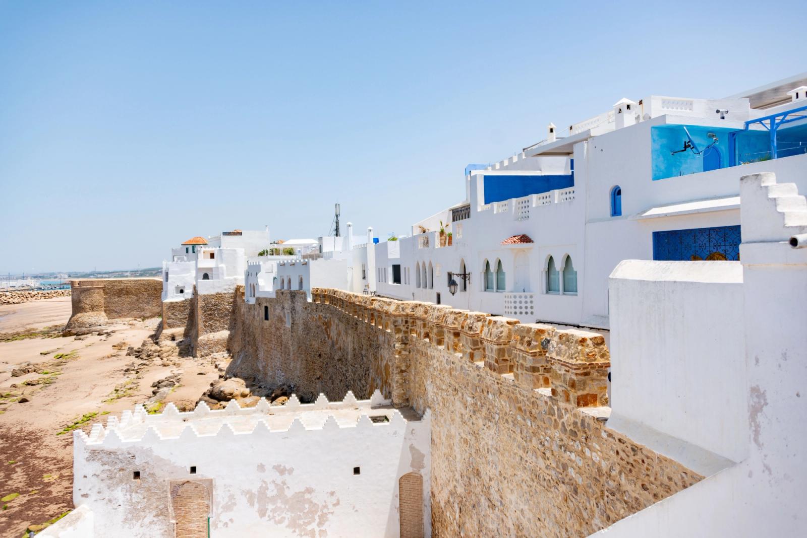 A view of a whitewashed medina with an ancient seaside fortress under a clear blue sky in Morocco