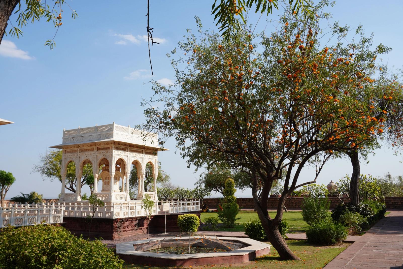 Beautiful white pavilion surrounded by lush greenery and vibrant blossoms in a serene Indian garden
