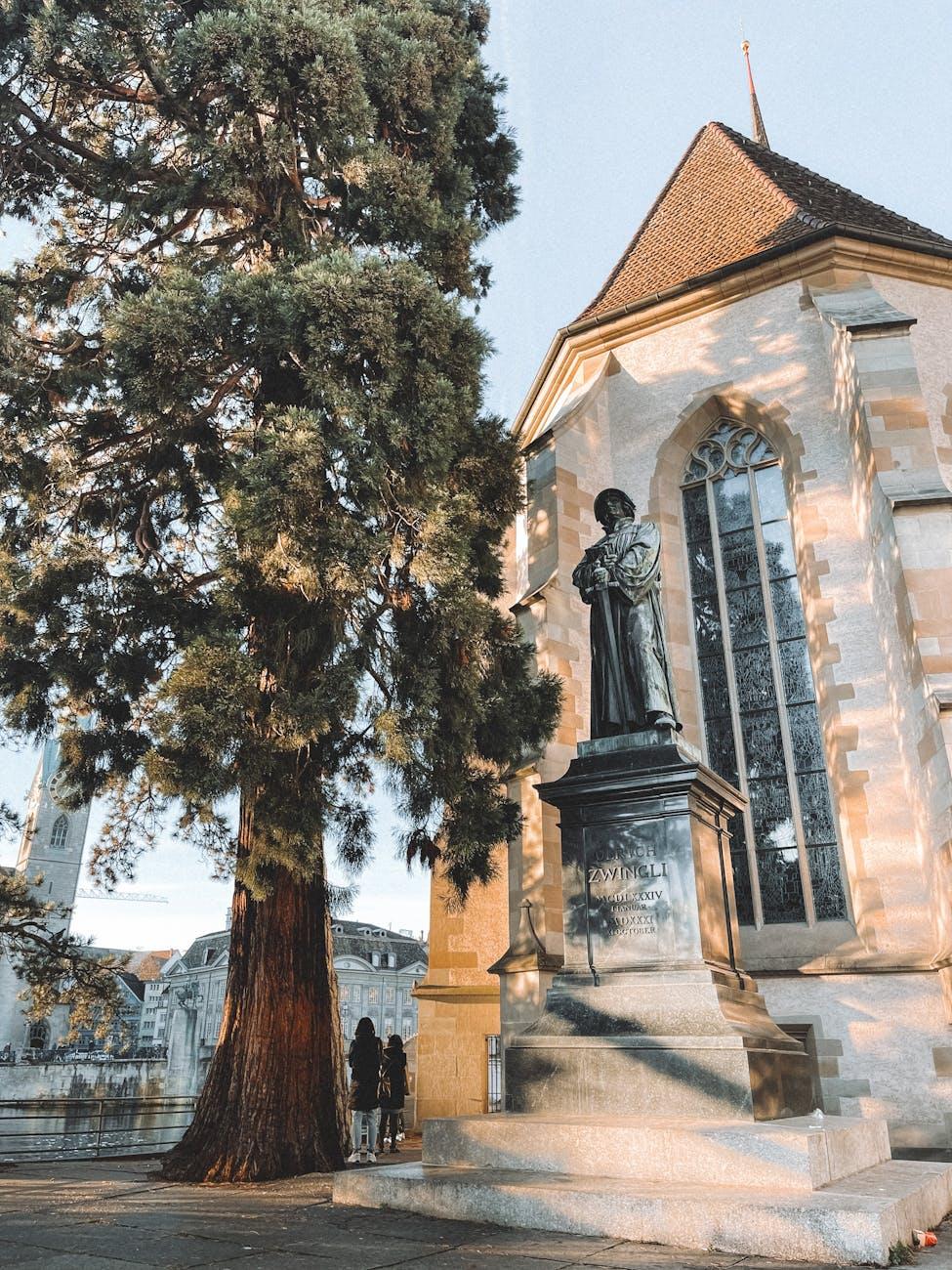 The Ulrich Zwingli monument stands beside a historic church in Zurich, Switzerland