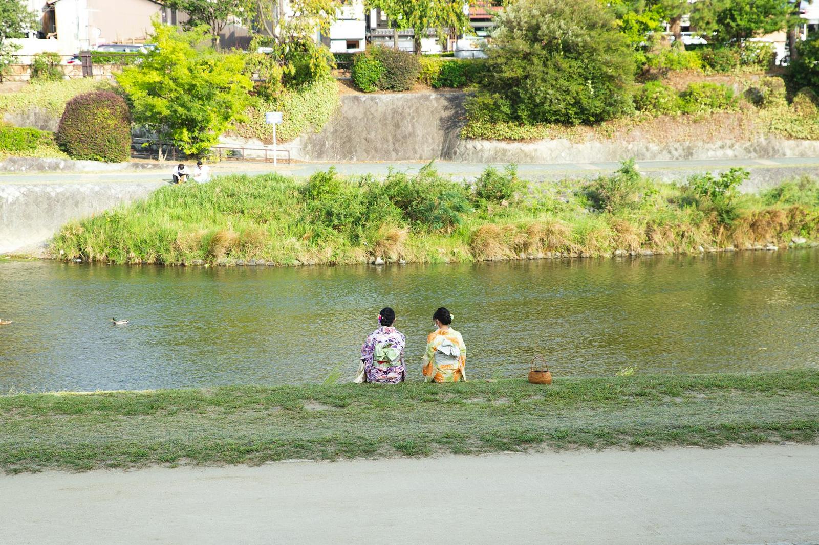Back view of anonymous ethnic women in traditional kimono apparels contemplating rippled river from coast in town