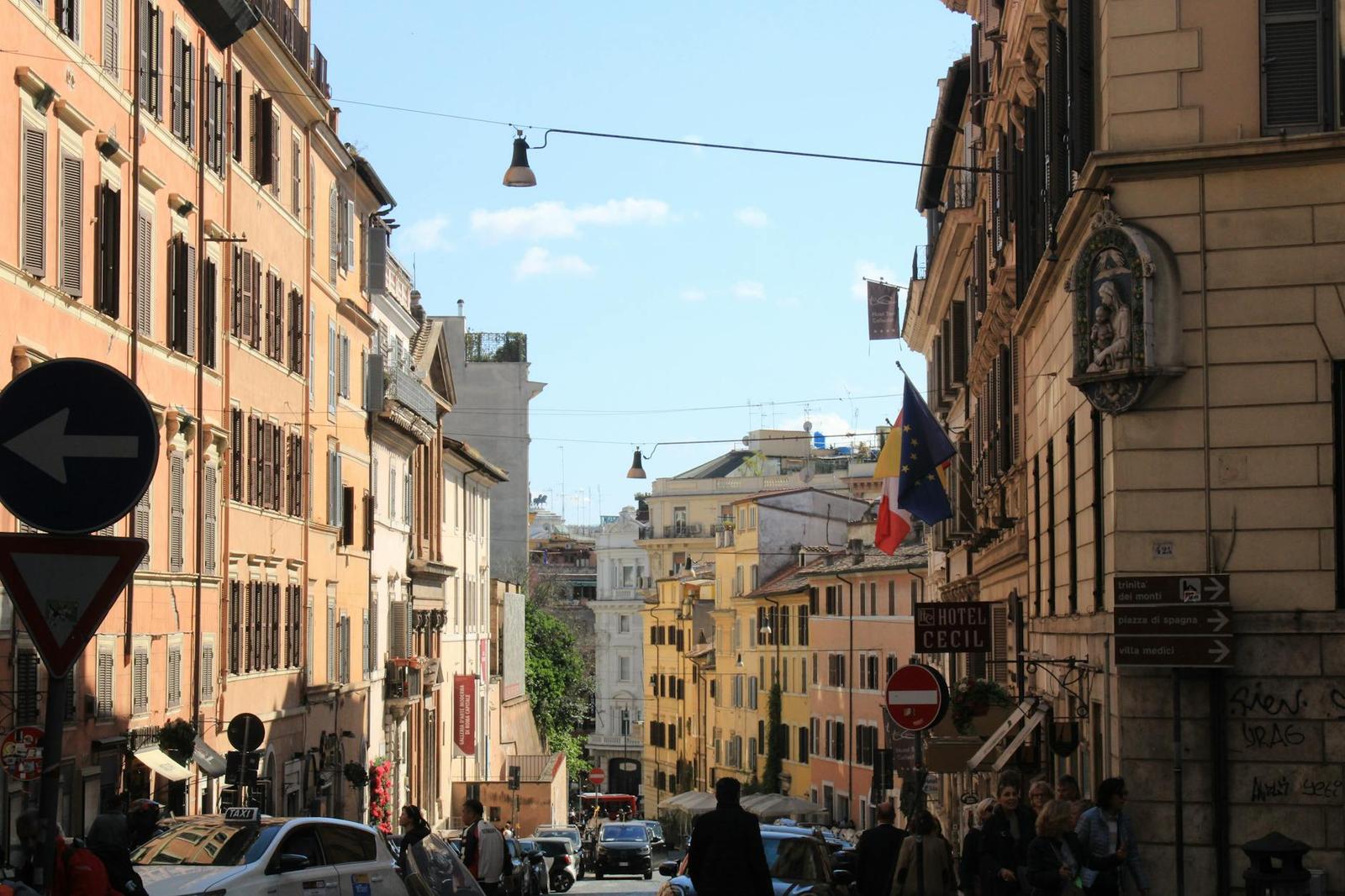 A busy city street lined with ochre buildings, traffic signs and pedestrians