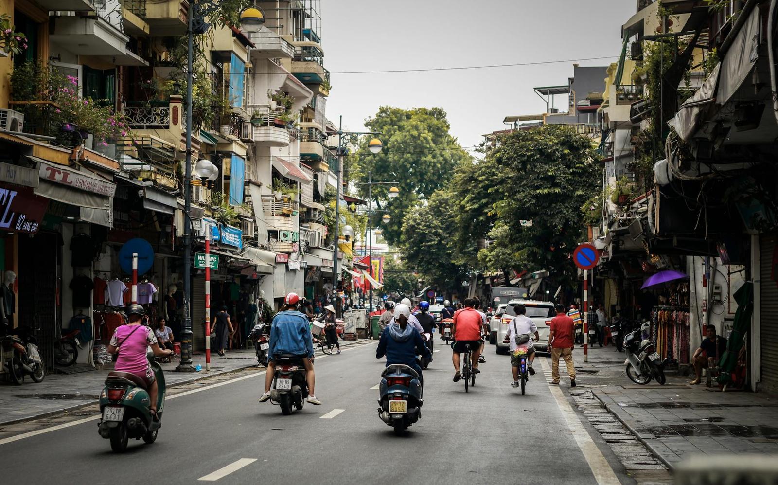 Cyclists and motorbikes riding down a tree-lined old quarter street